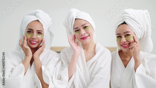 Close face group of beautiful young asian women in bathrobe and towels on heads with collagen patch on under eyes smiling to camera. Self care and daily beauty routine