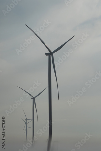 Windmills with rotor blades producing renewable ecological energy. Windmills turbines covered with morning fog low angle shot
