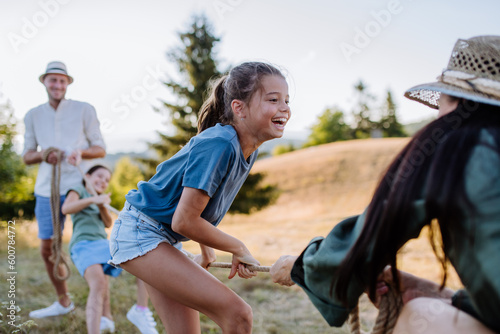 Young family with happy kids having fun together outdoors pulling rope in summer nature.