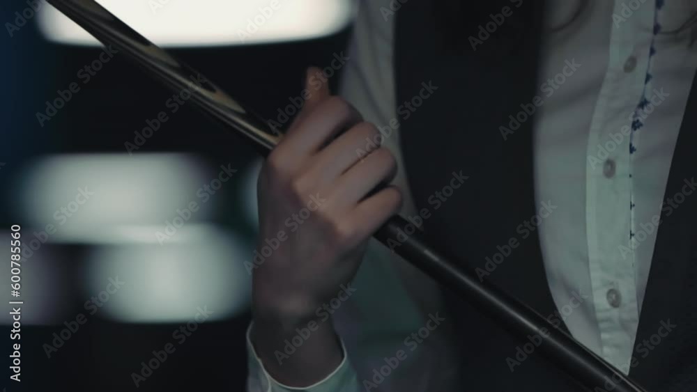 A young girl collects a cue. She is going to play billiards or snooker. In the background are the lamps of other tables. A young girl collects a cue. She is going to play billiards or snooker. In the background are the lamps of other tables.