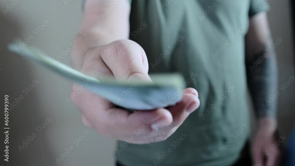 A man in a gray T-shirt holds out money to pay for the purchase. Man giving money. Financial business concept. Close up man's hand gives money dollars. A man in a gray T-shirt holds out money to pay for the purchase. Man giving money. Financial business concept. Close up man's hand gives money dollars.