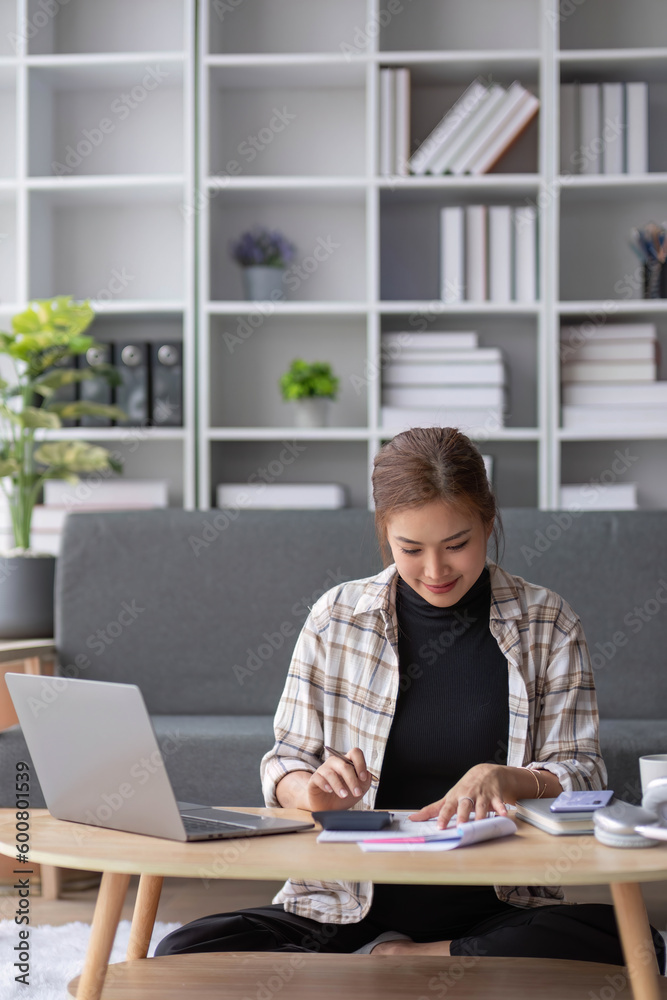 Attractive Asian female freelancer planning her project, working on her tasks on laptop computer at a coffee table in her living room.