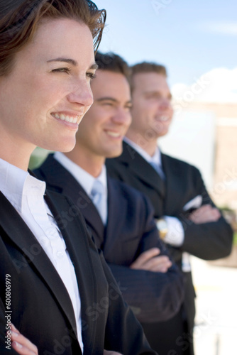 one female two males wearing dark business suits in a row smiling