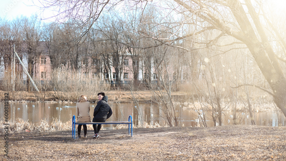 A pair of young people met in the park. Lovers are sitting on a bench in the city autumn park. An Asian boy and a white girl sitting on a park bench.