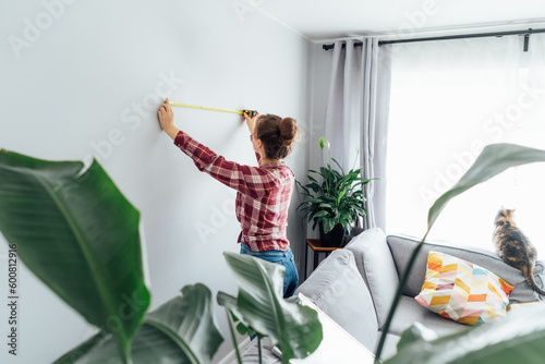 Fotografi Young woman doing measuring with a measure tape on the wall
