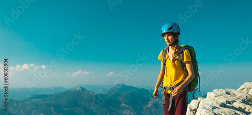 Woman climber with backpack and helmet enjoys amazing mountain view before climbing on a summer day. adventure and mountaineering concept. hiking with a backpack in the mountains.