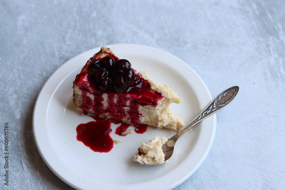 Slice of cheesecake with berry sauce on white plate. Homemade cheesecake with blackcurrant jam on top. Sweet food close up photo. Space for text. Slice of cheesecake with berry sauce on white plate. Homemade cheesecake with blackcurrant jam on top. Sweet food close up photo. Space for text.