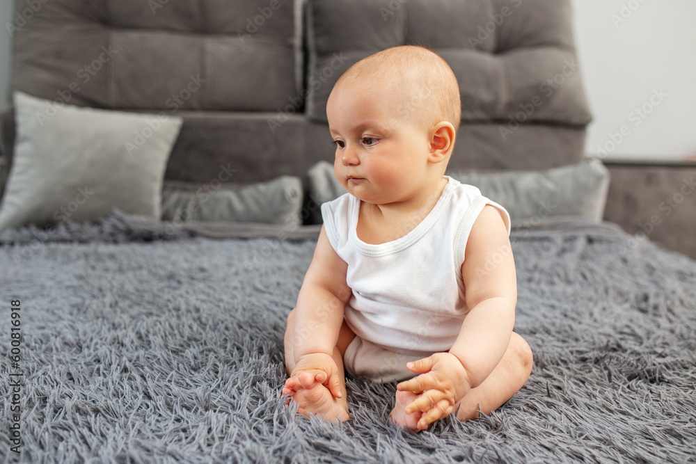 Little baby boy or girl sitting on bed at home. Childhood, babyhood and care concept.