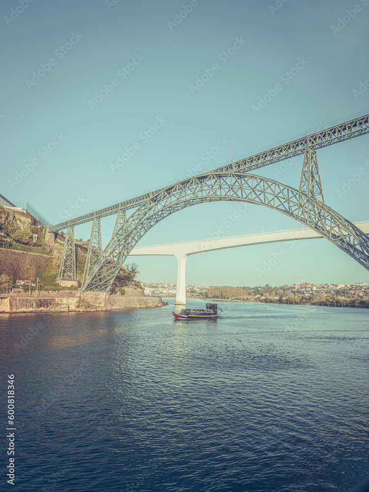Douro river with traditional sailing wine boat cruise, view of Maria Pia and Sao Joao bridges, typical architecture of cascade housing in sunhine. Rabelo boat in douro river, Porto, Portugal