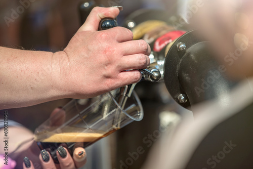 The bartender pours craft beer from the tap into a glass. The hand at the beer tap pours draft beer into a glass at the bar.