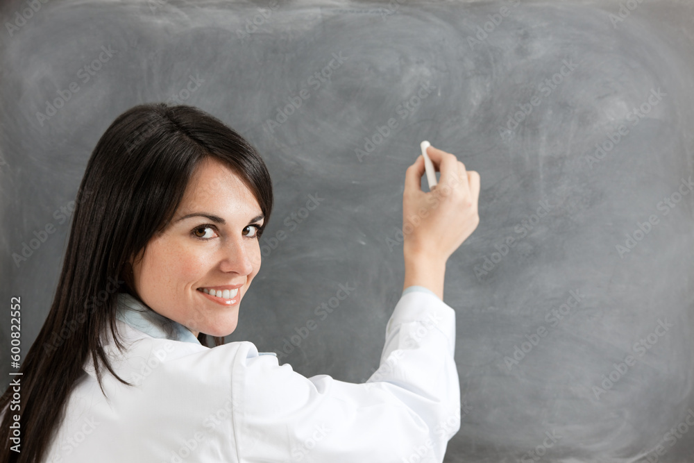 rear view of female teacher in lab clothes holding chalk against blank blackboard. Copy space rear view of female teacher in lab clothes holding chalk against blank blackboard. Copy space