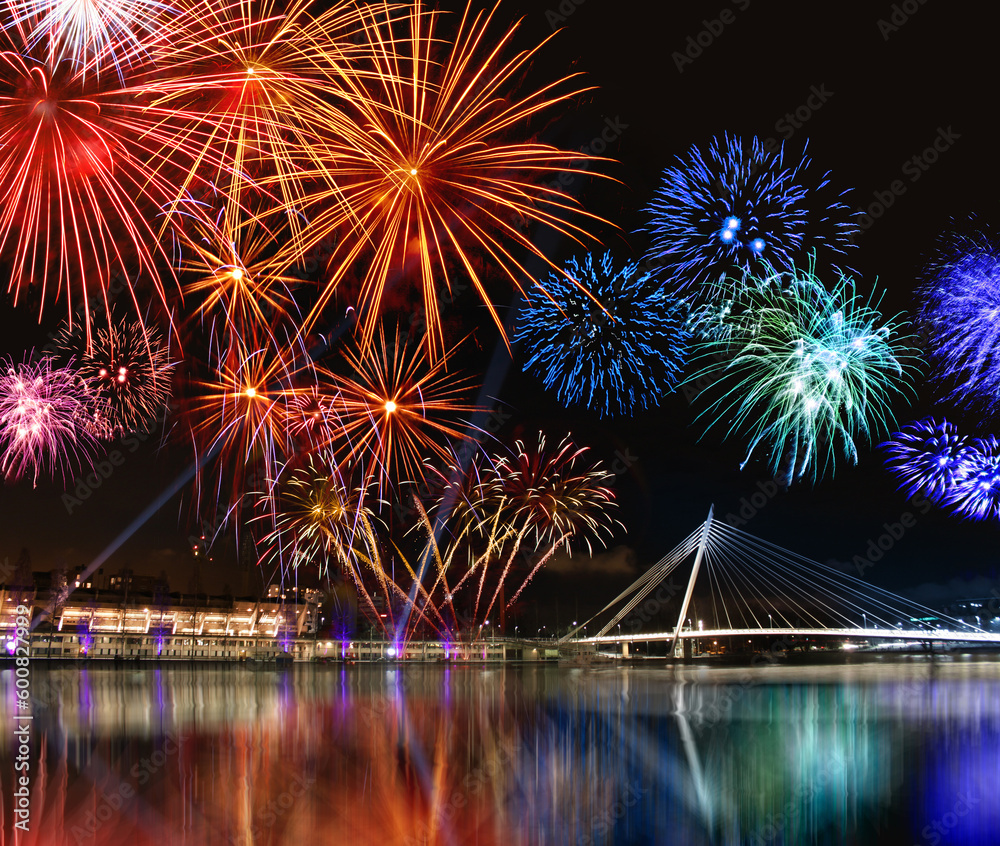 Fototapeta premium Colorful fireworks reflect from water, beautiful bridge scenery