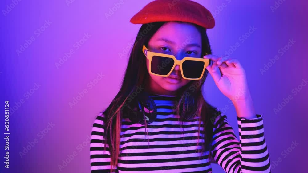 Asian Gen Z teenage girl with headphones, sunglasses and red hat with blue and red neon lights. Asian Gen Z teenage girl with headphones, sunglasses and red hat with blue and red neon lights.
