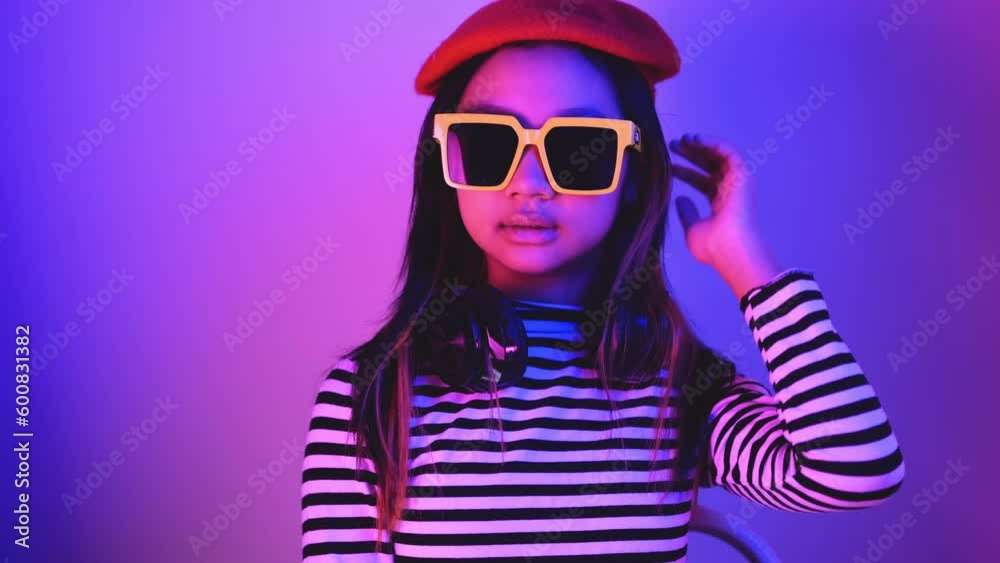 Asian Gen Z teenage girl with headphones, sunglasses and red hat with blue and red neon lights. Asian Gen Z teenage girl with headphones, sunglasses and red hat with blue and red neon lights.