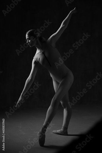 Ballerina in a beige bodysuit and pointe shoes. Dark background. Sculpted beautiful female body. Pose of a gymnast.