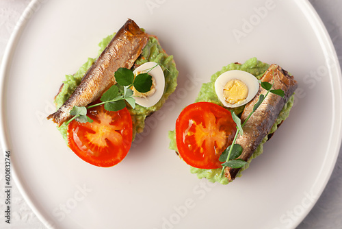 Sandwiches with sprats on toasted slices of bread. Sandwich with smoked sprat - fish, avocado and tomato. photo