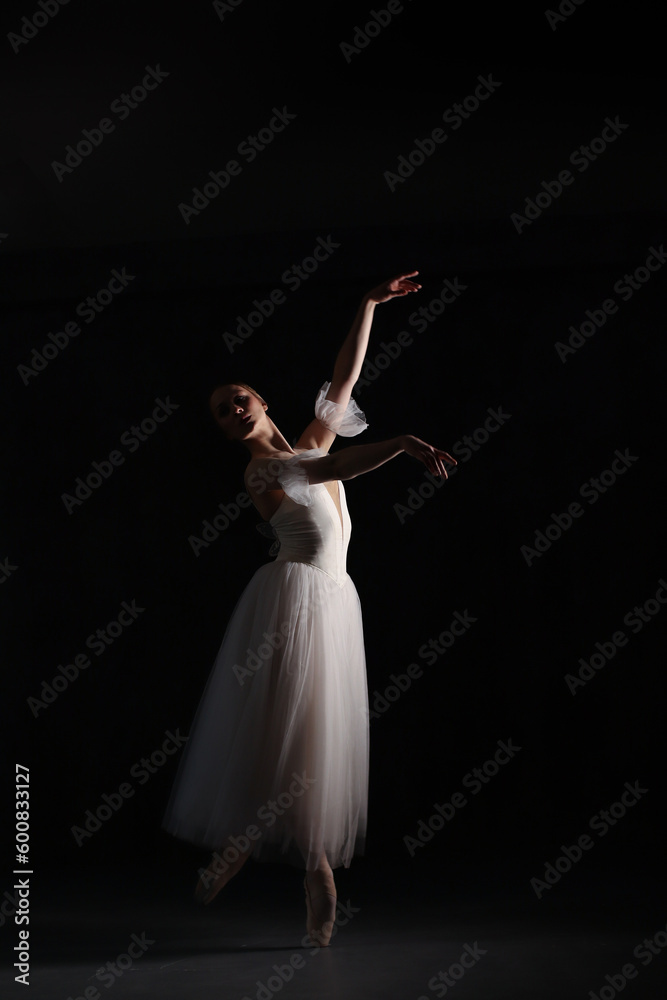 Professional ballerina dancing ballet.Ballerina in a white dress and pointe shoes. Dark background. Beautiful female body.