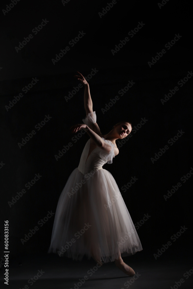 Fototapeta premium Professional ballerina dancing ballet.Ballerina in a white dress and pointe shoes. Dark background. Beautiful female body.