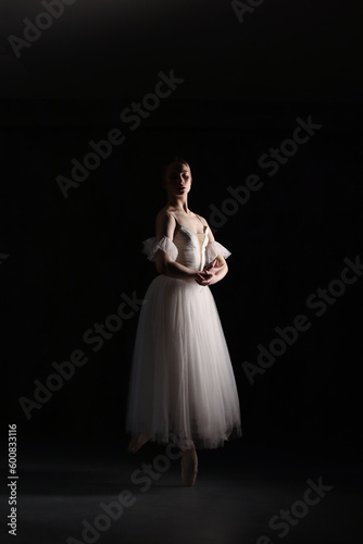 Professional ballerina dancing ballet.Ballerina in a white dress and pointe shoes. Dark background. Beautiful female body.