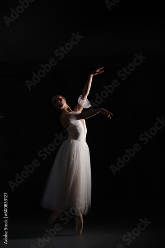 Professional ballerina dancing ballet.Ballerina in a white dress and pointe shoes. Dark background. Beautiful female body.