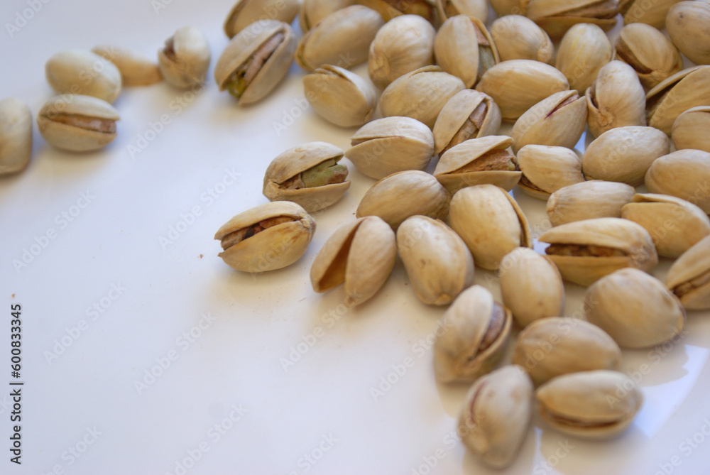 A handful of pistachios are scattered on the table. The shell of the nuts is half-open. They lie on a white plate.