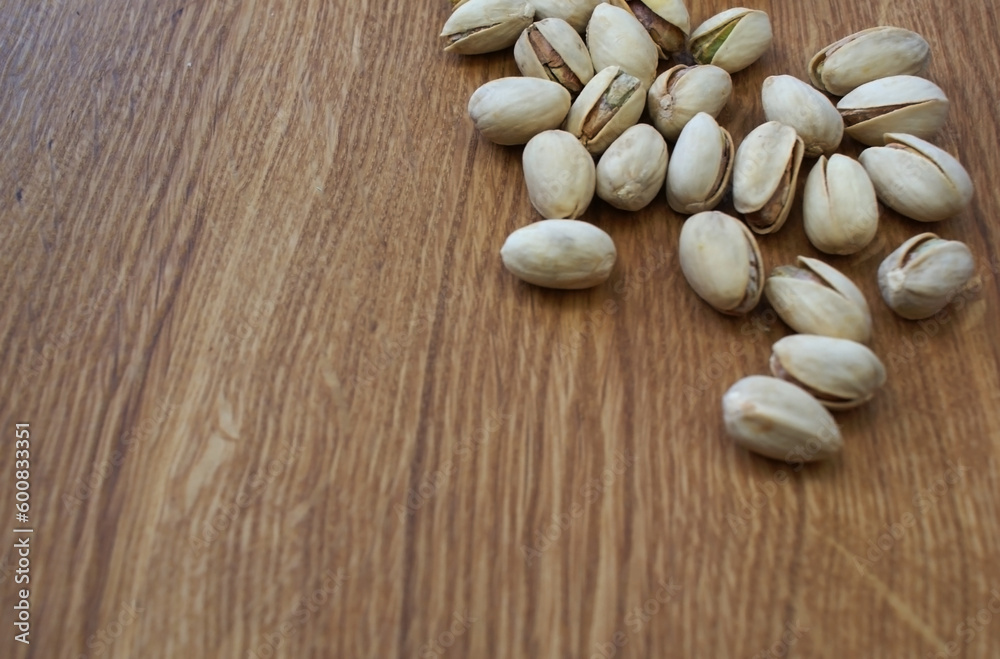 A handful of pistachios are scattered on the table. The shell of the nuts is half-open. They lie on a white plate.