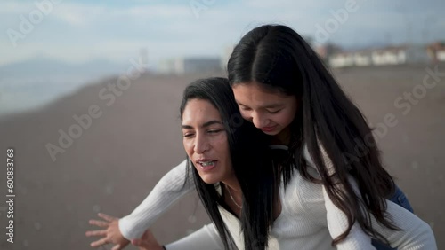 mother and daughter having fun piggyback spinning laughing on the beach	