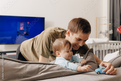 Young father plays with small one year old daughter girl with toy car indoor
