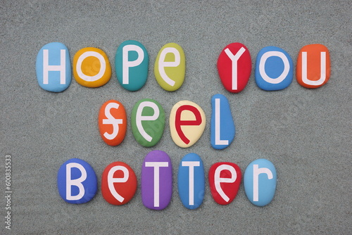 Hope you feel better, friendly message composed with multi colored stone letters over green sand
