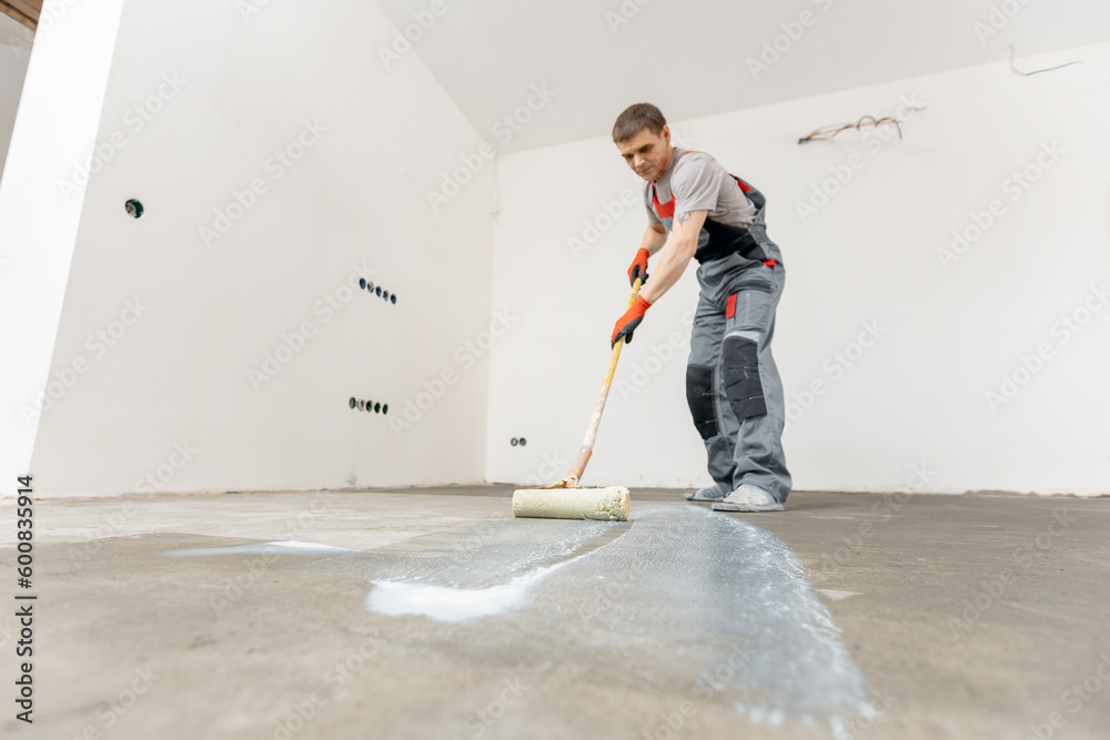 Floor priming process. Worker use primer on concrete floor before
