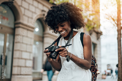 Wallpaper Mural Young black female tourist enjoys walking through the streets of a beautiful European city. She is happy and using her photo camera to take fantastic architecture photographs. Bright sunny day. Torontodigital.ca