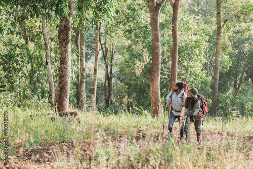Travelers hiking with backpack traveling in forest wild and look around and explore while walking in nature wood. happy holiday vacation trip. © NewSaetiew
