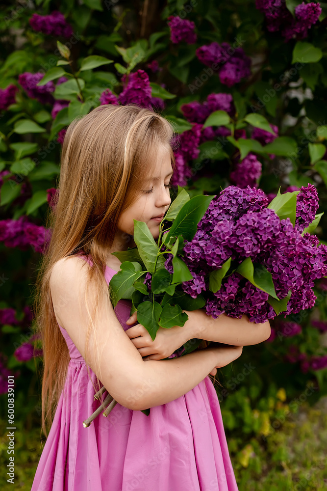 a beautiful happy smiling blonde girl with long hair in a pink dress with a purple bouquet of lilacs in her hands stands against the background of a lilac bush a beautiful happy smiling blonde girl with long hair in a pink dress with a purple bouquet of lilacs in her hands stands against the background of a lilac bush