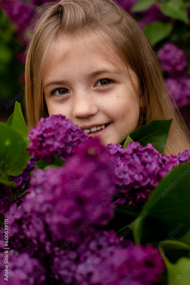 a beautiful happy smiling blonde girl with long hair in a pink dress with a purple bouquet of lilacs in her hands stands against the background of a lilac bush a beautiful happy smiling blonde girl with long hair in a pink dress with a purple bouquet of lilacs in her hands stands against the background of a lilac bush