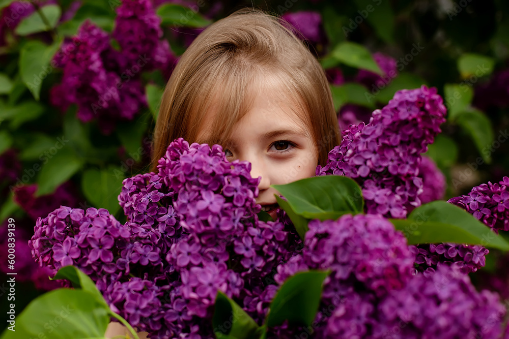 a beautiful happy smiling blonde girl with long hair in a pink dress with a purple bouquet of lilacs in her hands stands against the background of a lilac bush a beautiful happy smiling blonde girl with long hair in a pink dress with a purple bouquet of lilacs in her hands stands against the background of a lilac bush