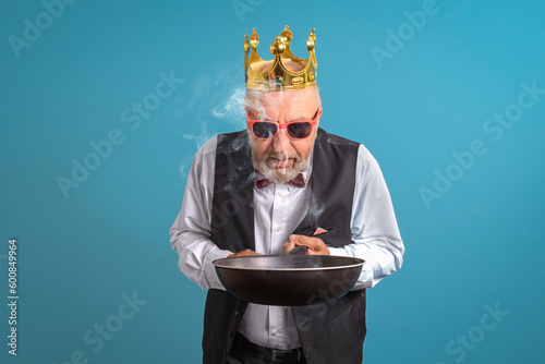 King of kitchen. A man in gold corona with a burnt frying pan in his hand. On a blue background