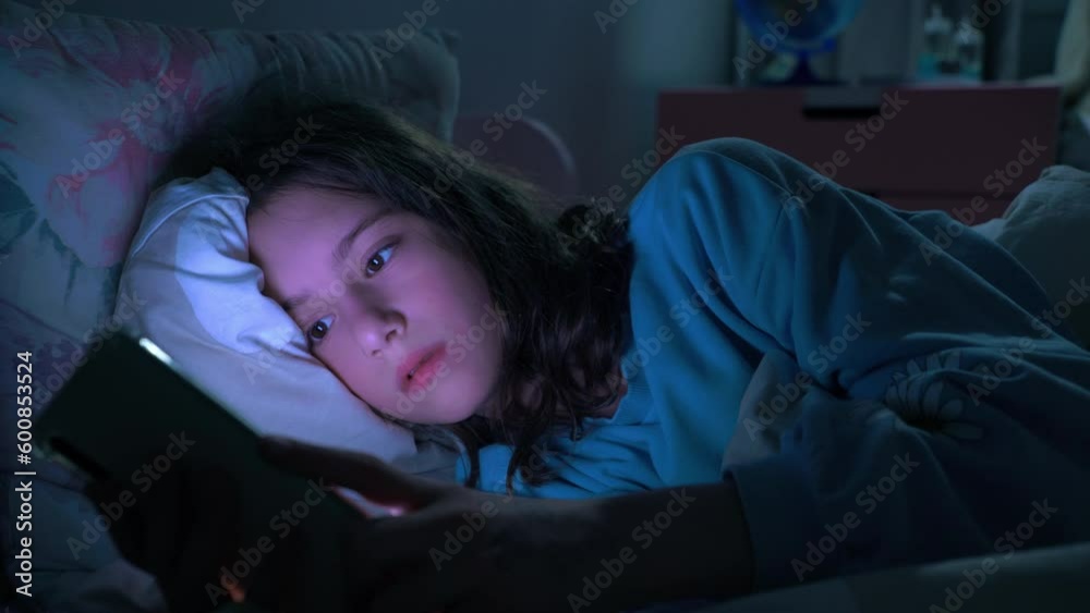 Teen girl scrolling social media texting on smartphone in bed in bedroom at night. Technology, internet, communication and people concept. Dependence on social networks in children. Not healthy sleep.