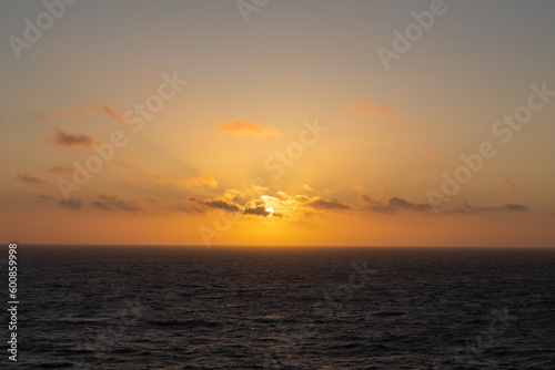 An orange sunset over the sea with light clouds.
