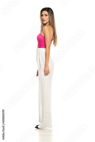 Side view of a young modern woman in white pants and pink corset posing on white background