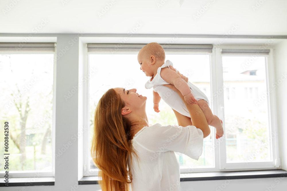 Happy cheerful young mother throws an adorable baby in air, plays, hugs baby with love, care Happy cheerful young mother throws an adorable baby in air, plays, hugs baby with love, care