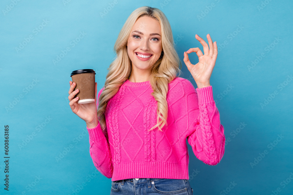 Fototapeta premium Photo of good mood pretty girl with wavy hairdo dressed pink sweater showing okey hold cup of latte isolated on blue color background