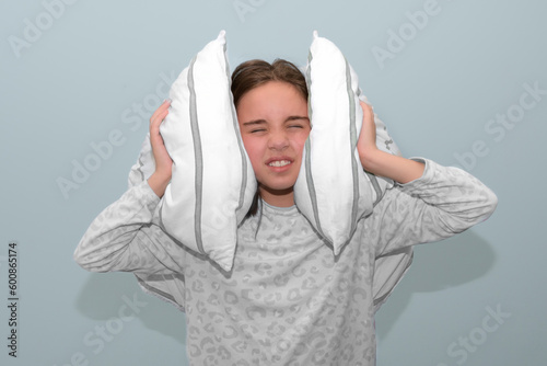The girl covers her ears with pillows from a loud sound. Insomnia in teenagers. portrait studio. Girl can't sleep.