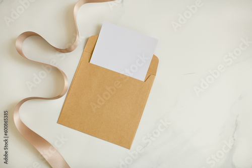 Flay Lay Photo of Blank Empty White Paper in Brown Paper Envelope on Marble Countertop with Rose Gold Silk Ribbon