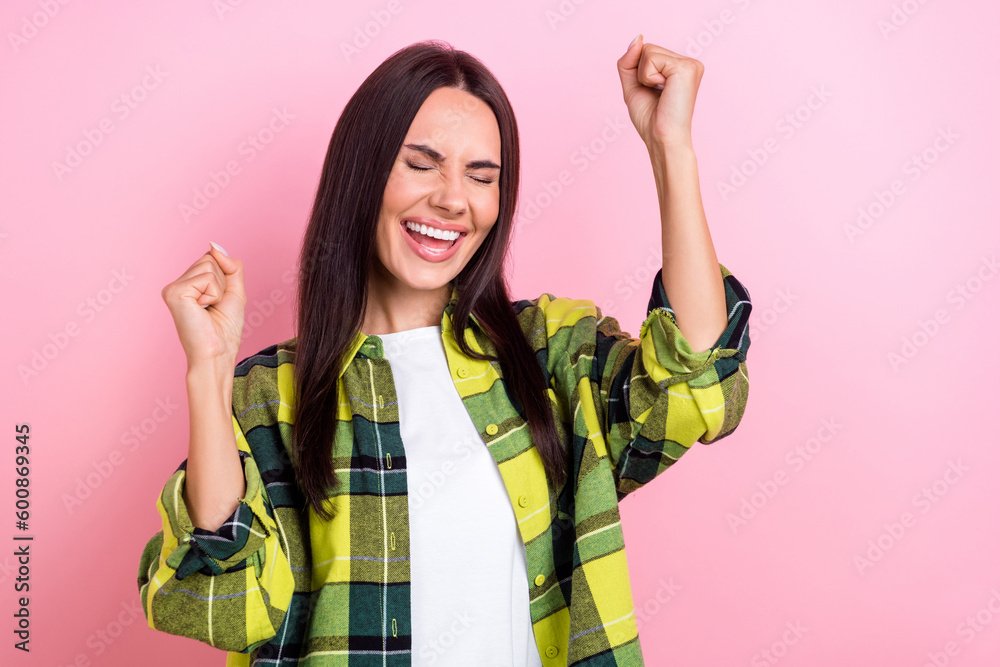 Photo of lucky excited woman dressed plaid shirt rising fists empty space isolated pink color background Photo of lucky excited woman dressed plaid shirt rising fists empty space isolated pink color background