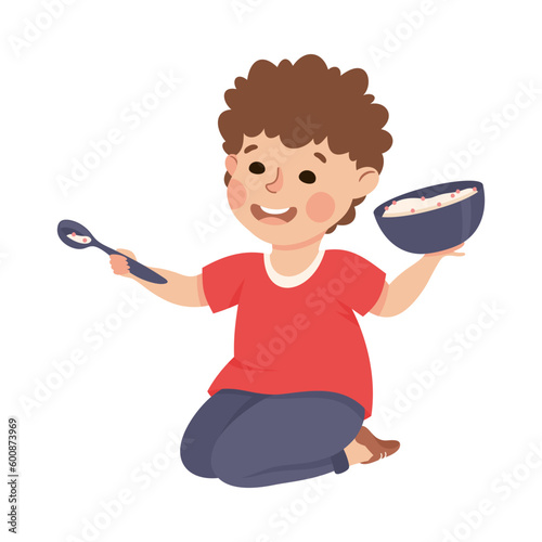 Cute preschool little boy sitting on floor holding bowl of porridge and spoon cartoon vector illustration
