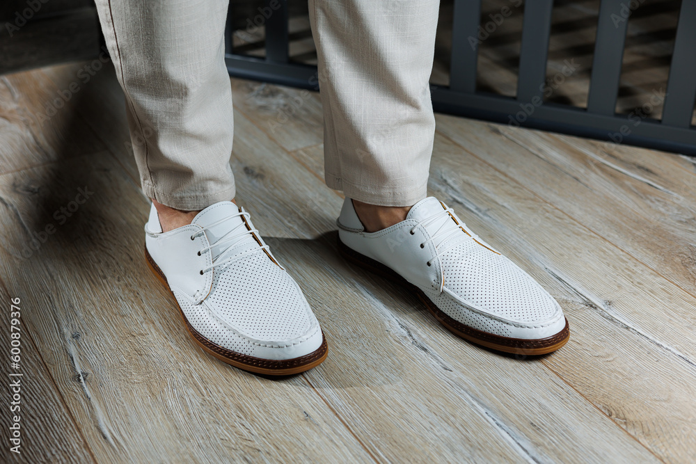 Male feet close-up in white casual shoes. Fashionable young man standing in leather stylish white moccasins in trousers. Seasonal summer men's shoes. Casual street style. Male feet close-up in white casual shoes. Fashionable young man standing in leather stylish white moccasins in trousers. Seasonal summer men's shoes. Casual street style.