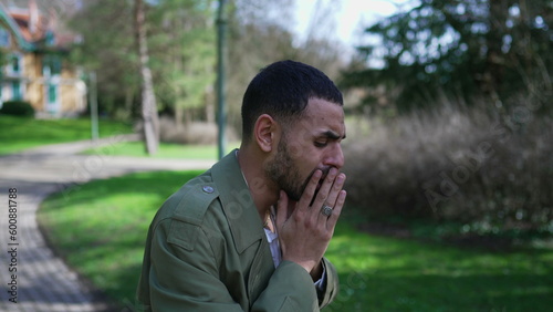 Troubled man covering face in shame and anxiety. A Desperate depressed Middle Eastern person stands outdoors at park feeling worry and preoccupation © Marco