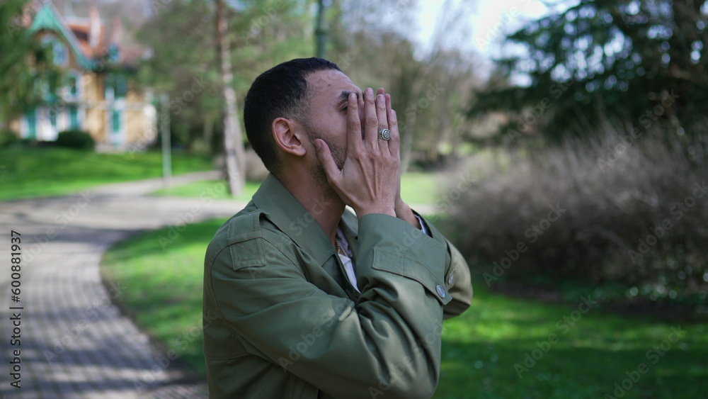 Troubled man covering face in shame and anxiety. A Desperate depressed Middle Eastern person stands outdoors at park feeling worry and preoccupation Troubled man covering face in shame and anxiety. A Desperate depressed Middle Eastern person stands outdoors at park feeling worry and preoccupation