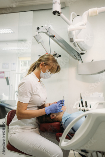 European mid pleased dentist woman in face mask working in dental clinic.