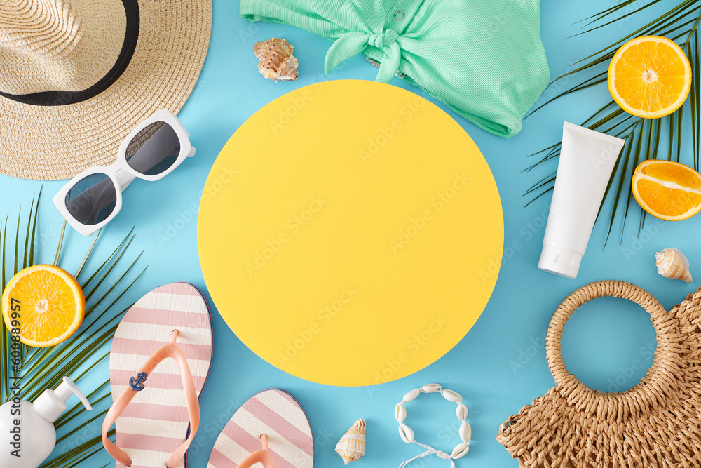 Beach vacation concept. Top view flat lay of stylish swimsuit, bag, flip-flops, sunhat, accessories, orange slices and palm leaves on light blue background with blank yellow circle for text or advert Beach vacation concept. Top view flat lay of stylish swimsuit, bag, flip-flops, sunhat, accessories, orange slices and palm leaves on light blue background with blank yellow circle for text or advert